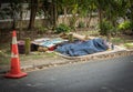 Homeless asleep on roadside by orange road cone