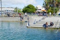 People walk along harbor edge Tauranga city waterfront playground and The Strand background.