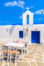 Tavern tables in front of typical white Greek church in Naoussa port, Paros island, Cyclades, Greece Royalty Free Stock Photo