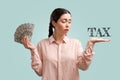 Tax and accounting. A thoughtful young pretty Caucasian woman holds a fan of dollars and looks at left palm. Turquoise