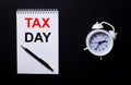 TAX DAY is written in a white notepad near a white alarm clock on a black background Royalty Free Stock Photo