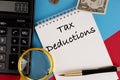 Tax deductions, the text is written in a white notepad, next to a calculator, a pen and a magnifying glass