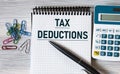 TAX DEDUCTIONS - words on a notebook on a light wooden background with a calculator and a pen