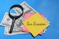 Tax evasion wording with magnifying glass and bank note over a blue background. Economy concept Royalty Free Stock Photo