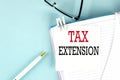 TAX EXTENSION text on a sticky on notebook with pen and glasses , blue background