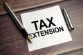 TAX EXTENSION text on sticky with pen and wooden background