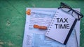 Tax-filling concept - TAX TIME text on notebook with the U.S IRS 1040 form,coins,pen and eyeglasses in vintage background