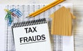 TAX FRAUDS - words in a notebook against the background of a house, pencils and paper clips Royalty Free Stock Photo