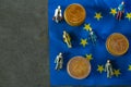 Figurines of people and euro coins on European union flag.