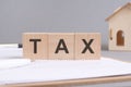 TAX text made of wooden blocks on gray background with a small wooden model house Royalty Free Stock Photo