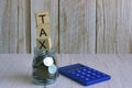 Tax text on wooden block cube on top of glass jar with multicurrency coins