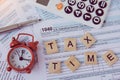 Tax time with wooden alphabet blocks, red alarm clock, calculator and pen on 1040 tax form backgrounda Royalty Free Stock Photo