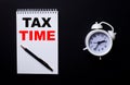 TAX TIME is written in a white notepad near a white alarm clock on a black background. Tax concept Royalty Free Stock Photo