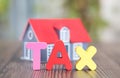 Tax word made of English letter model and small house model blurred behind