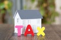 Tax word made of English letter model and small house model blurred behind