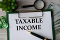 TAXABLE INCOME - words on a white sheet against the background of banknotes, magnifying glass and cactus