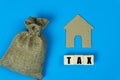 Taxation and Annual tax concept. A message on wooden block with a small house paper cut and money bag  on blue background Royalty Free Stock Photo