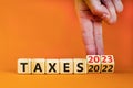 2023 taxes new year symbol. Businessman turns a wooden cube and changes words Taxes 2022 to Taxes 2023. Beautiful orange table