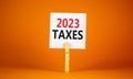 2023 taxes new year symbol. White paper with words 2023 taxes, clip on wooden clothespin. Beautiful orange table orange background