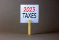 2023 taxes new year symbol. White paper with words 2023 taxes, clip on wooden clothespin. Beautiful grey table grey background.