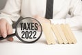 TAXES 2022 text wooden cube blocks and hand holding magnifying glass on table Royalty Free Stock Photo