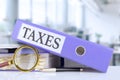 Taxes, text written in a folder with documents in trendy purple color, lying on a stack of papers, documents on an office desk and Royalty Free Stock Photo