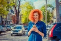 Taxi app. Pretty happy smiling urban woman using smart phone, standing on city street on sunny day waiting for taxi. Beautiful Royalty Free Stock Photo