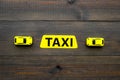 Taxi concept. Yellow service sign text taxi near car toy on dark wooden background top view copy space
