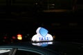 Taxi light sign or cab sign in blue and white color on the car roof at the street in the dark night