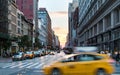 Taxi speeding through the intersection of 23rd Street and 5th Avenue with the colorful light of sunset in the background of the Ma