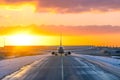 Taxiing aircraft on tarmac taxiway towards the rusting orange sun in winter