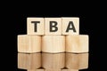 TBA text assembled from wooden cubes on a black background