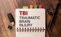 Concept words TBI traumatic brain injury on white note on a beautiful black background. Pencil and pen Royalty Free Stock Photo