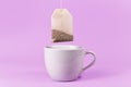 Tea bag hanging above white tea cup on purple background Royalty Free Stock Photo