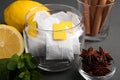 Tea bags, anise stars, cinnamon sticks, mint and lemon on grey wooden table, closeup