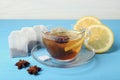 Tea bags, cup of hot drink, anise stars and lemon on light blue wooden table