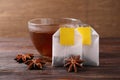 Tea bags, cup of hot drink and anise stars on wooden table, closeup