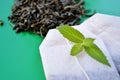 Tea bags, loose tea and fresh mint leaves on a green background