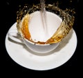 Tea being poured into a saucer with splashes on a black background Royalty Free Stock Photo