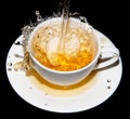 Tea being poured into a saucer with splashes on a black background Royalty Free Stock Photo