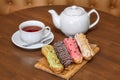 Tea and colorful eclair cakes with cream on wooden board Royalty Free Stock Photo