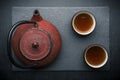 Tea composition with ceramic tea cups and red iron teapot on dark stone background Royalty Free Stock Photo