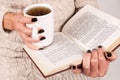 Tea cup and book in young women hands with black nails and sweater Royalty Free Stock Photo