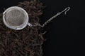 Tea filter on a chain with black tea on a pile of dry tea leaves. Tea filter - close-up of a kitchen accessory