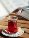 Tea in a glass cup armudu on a saucer. A piece of cane sugar and a spoon nearby. On the table is an open book, time for rest. Royalty Free Stock Photo