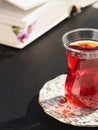 Tea in a glass cup armudu on a saucer. On the table is an open book, time for rest. Bright sunny day. Close-up Royalty Free Stock Photo