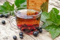 Tea in a glass cup of black currant on a wooden table near a glass teapot on a background of green grass Royalty Free Stock Photo