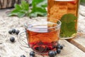 Tea in a glass cup of black currant on a wooden table near a glass teapot on a background of green grass Royalty Free Stock Photo