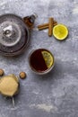 Tea in glass teacup with lemon. Near glass teapot, cinnamon sticks, jam in jar, hazelnuts and lemon at gray background