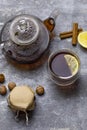 Tea in glass teacup with lemon. Near glass teapot, cinnamon sticks, jam in jar, hazelnuts and lemon at gray background